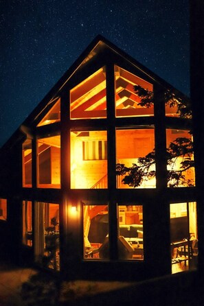 Una casa moderna de varios niveles, con amplios ventanales y un cálido resplandor interior.