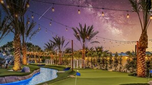 A golf course at dusk with string lights, palm trees, and a pool.