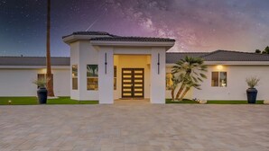 A modern house with a central entrance, surrounded by a paved driveway and potted plants.