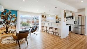 A modern kitchen with stainless steel appliances, a dining area with a cactus mural, and a large window offering a view of the mountains.