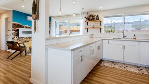 A modern kitchen with white cabinetry, pendant lighting, and a view of the outdoors.