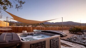 A hot tub with a wooden deck, surrounded by a wooden fence and a large shade sail.