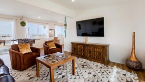 A spacious living room with a foosball table, two brown leather sofas, a wooden coffee table, a large TV, and a decorative vase.