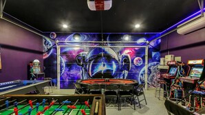 Ein Raum mit Fußballtisch, Billardtisch und einer Wandmalerei zum Thema Weltall.