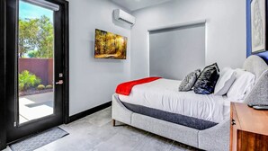 Ein Schlafzimmer mit einem Bett, einer Tür, einer Klimaanlage, einem Gemälde und einem Fenster.