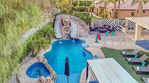A pool area with a waterfall feature, lounge chairs, and a covered seating area.
