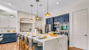 Une cuisine moderne avec un îlot en marbre, des chaises en bois et des armoires bleues.