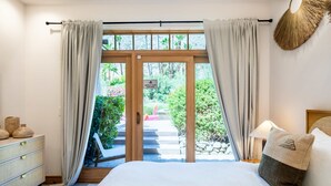 A bedroom with a bed, a dresser, a nightstand, a lamp, and a view of a garden through a glass door. - LUX - Historic Tennis Club Enclave - King Beds (Palm Springs)