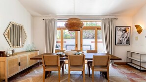 A dining area with a table set for four, a woven pendant light, a large mirror, and a window with curtains. - LUX - Historic Tennis Club Enclave - King Beds (Palm Springs)