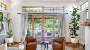 A living room with two leather sofas, a coffee table, and a view of an outdoor patio with chairs and a garden. - LUX - Historic Tennis Club Enclave - King Beds (Palm Springs)