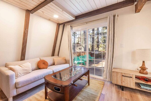 A cozy living room with a sofa, coffee table, and a view of outdoor seating through a large window.