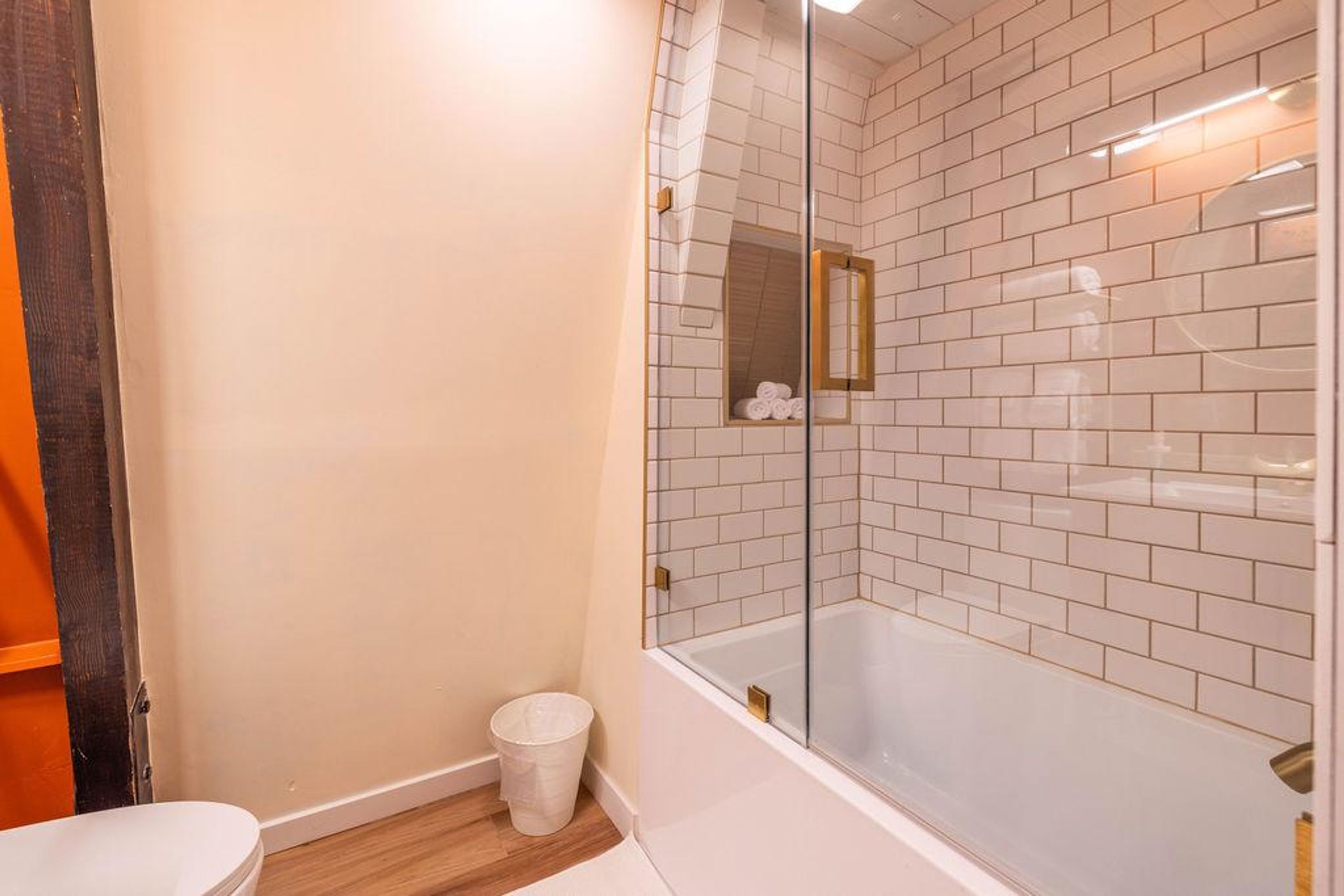 Ein Badezimmer mit Duschkabine, weißen Fliesen, einer weißen Toilette und Holzboden.
