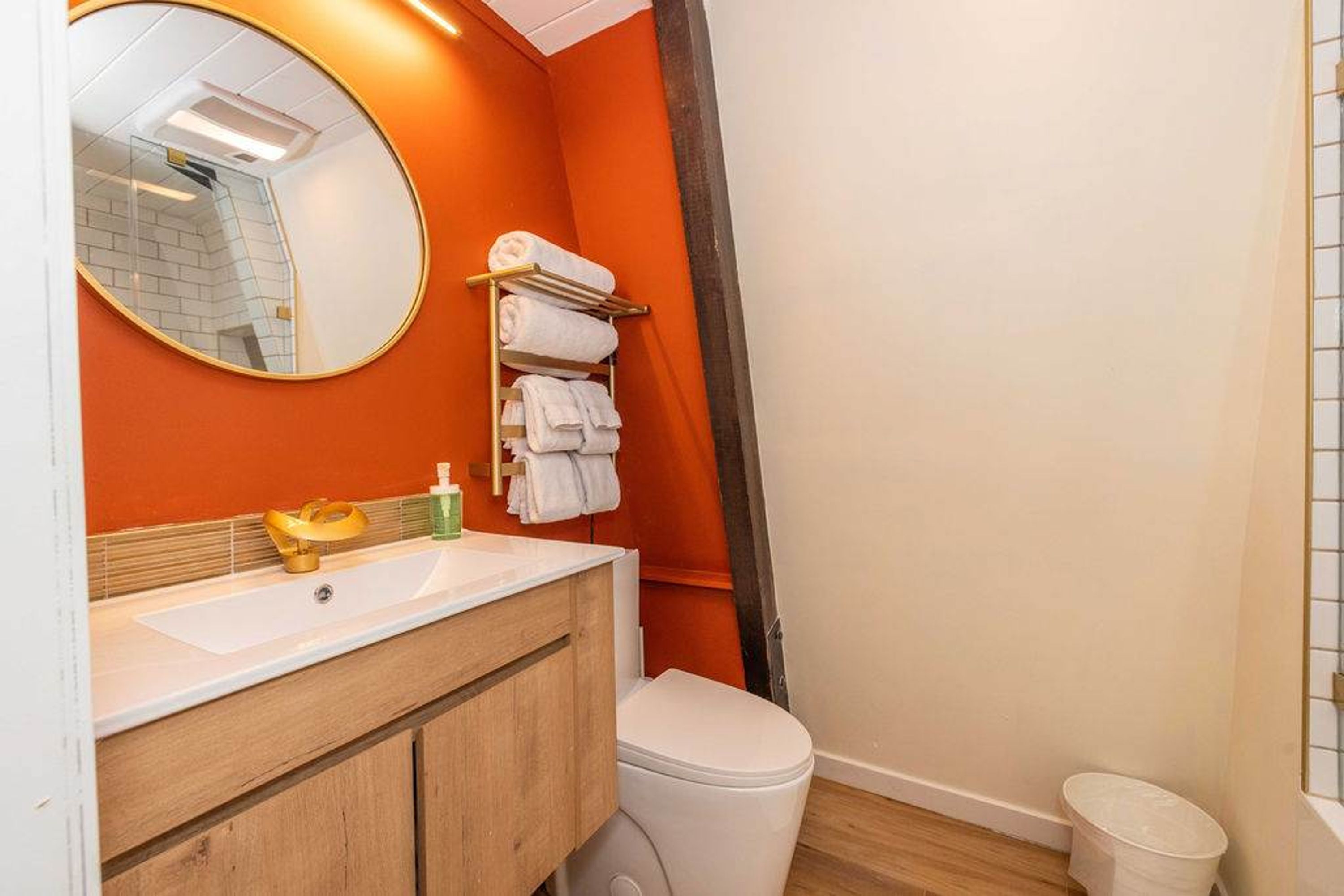Une salle de bain avec un lavabo blanc, un meuble-lavabo en bois, un miroir rond et des toilettes.