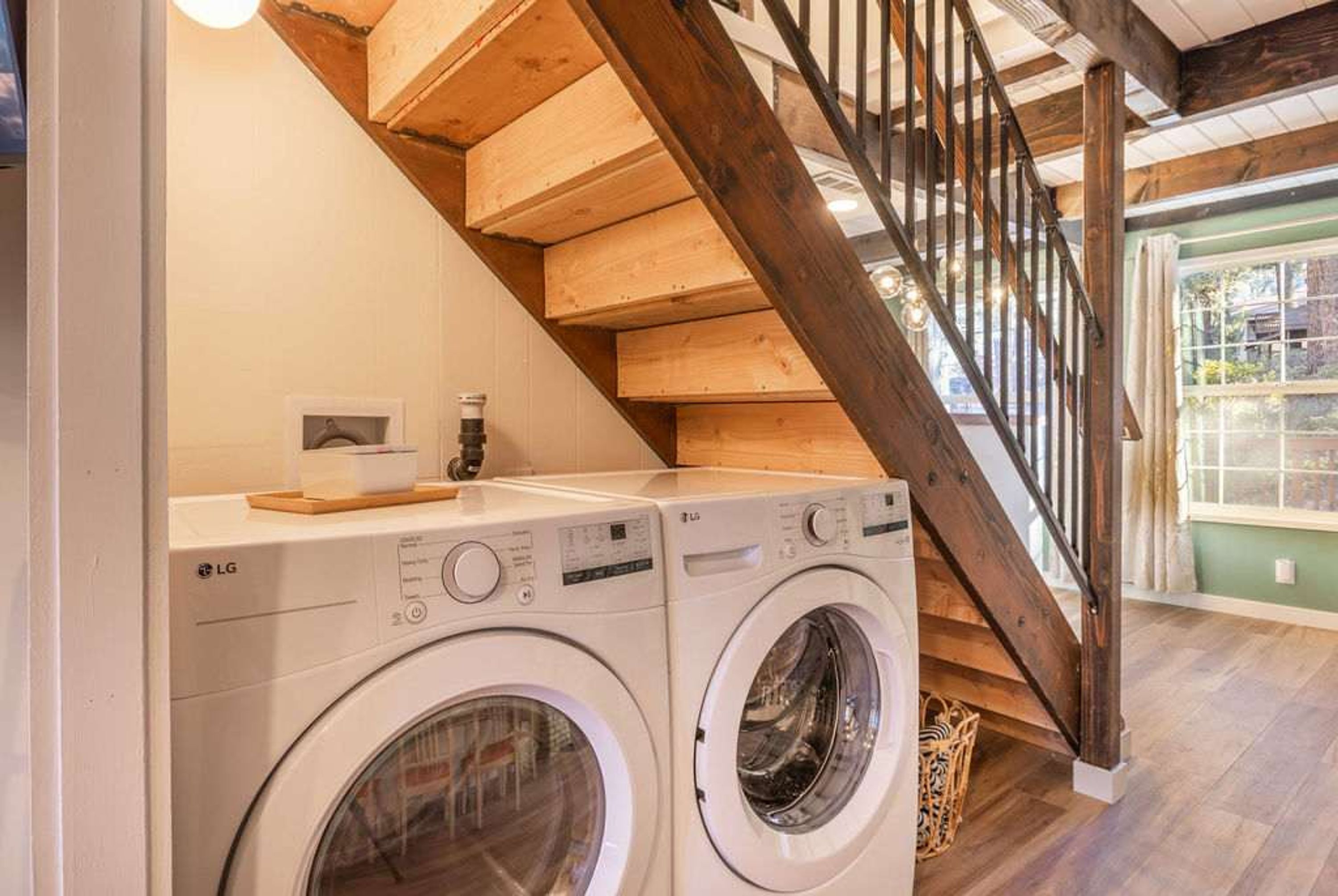 Un área de lavandería con dos lavadoras LG, una escalera de madera y vistas al exterior.