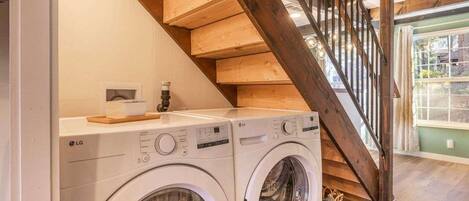 Un área de lavandería con dos lavadoras LG, una escalera de madera y vistas al exterior.