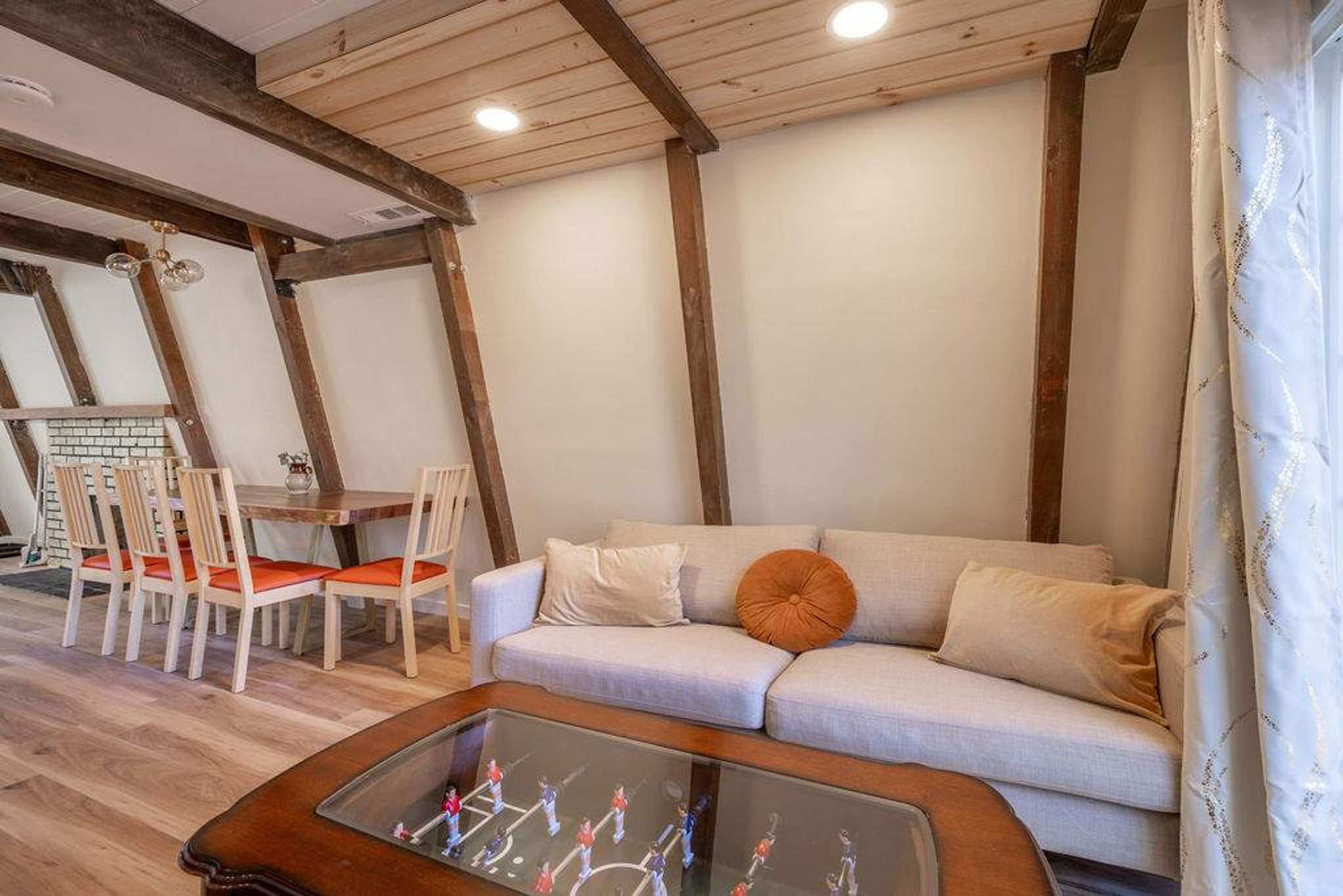 A cozy living room with a sofa, a coffee table with a board game, wooden beams on the ceiling, and a dining area with chairs and a table.