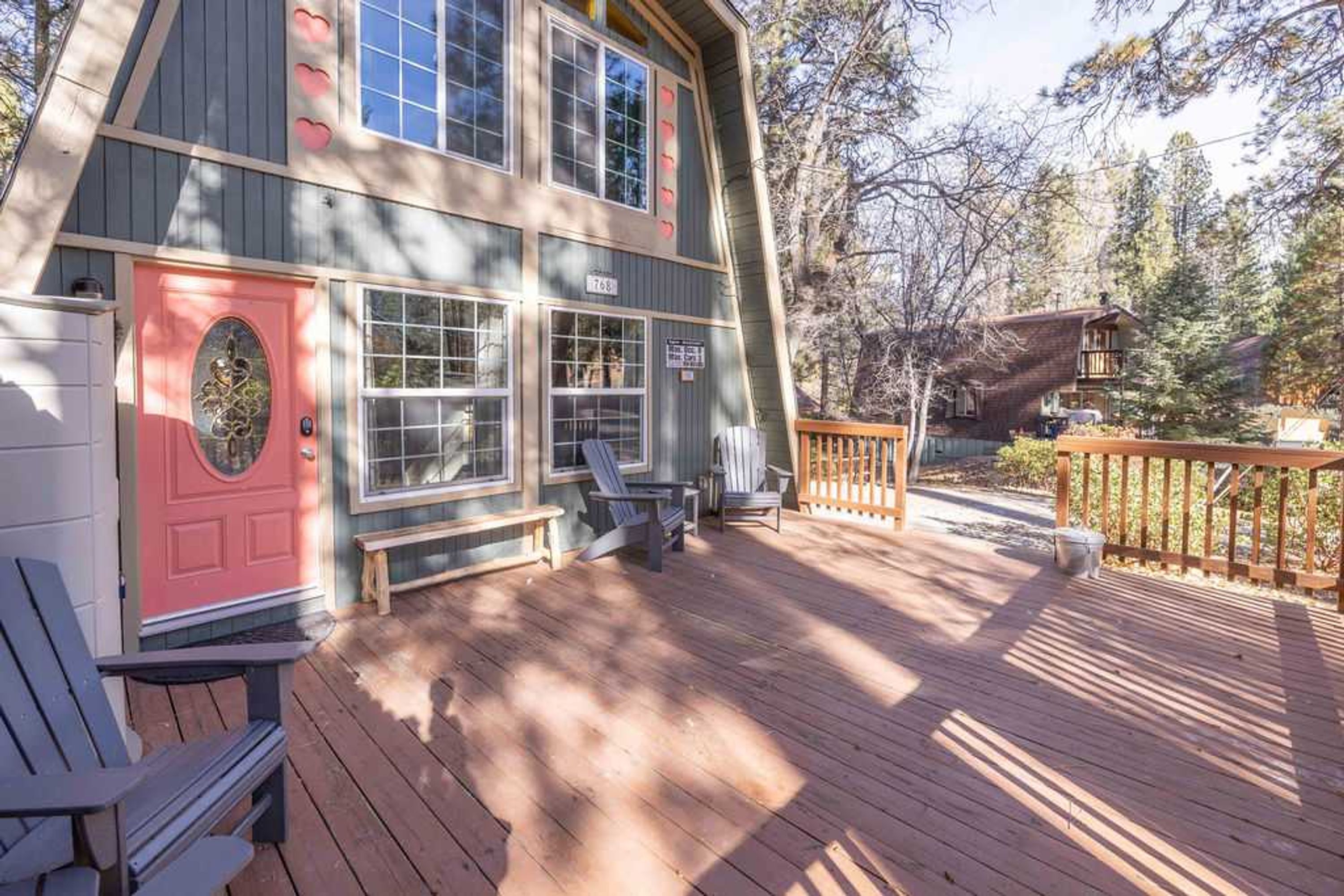 Une maison en bois à deux étages, avec une porte rose, une véranda dotée de fauteuils Adirondack et une terrasse en bois.