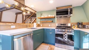 Una cocina moderna con armarios color turquesa, electrodomésticos de acero inoxidable y una escalera de madera.