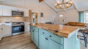 Cucina con mobili bianchi, isola in legno, forno a incasso e lampadario a sospensione.
