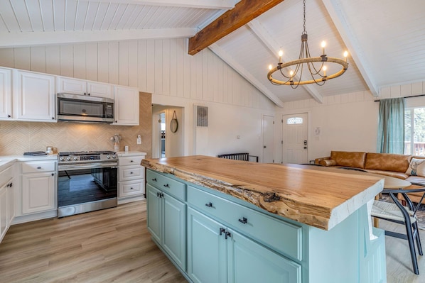 A kitchen with white cabinets, a wooden island, a built-in oven, and a hanging chandelier.