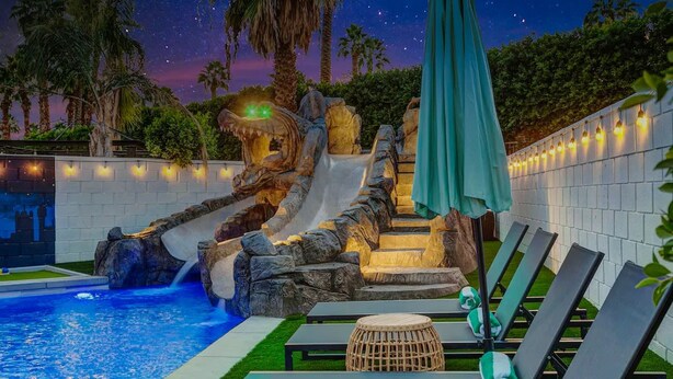 A poolside area with a slide, lounge chairs, and a starry night sky. - Forever Young Crocslide Pickleball 7BD Game Rm (Indio)