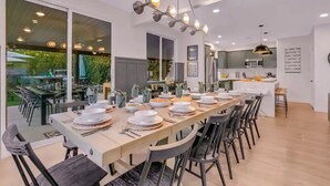 A modern dining area with a long table set for a meal, surrounded by chairs. - Forever Young Crocslide Pickleball 7BD Game Rm (Indio)