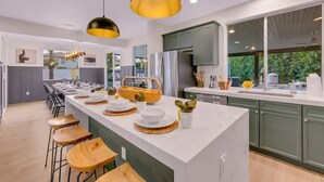 A modern kitchen with a central island, bar stools, and pendant lighting. - Forever Young Crocslide Pickleball 7BD Game Rm (Indio)