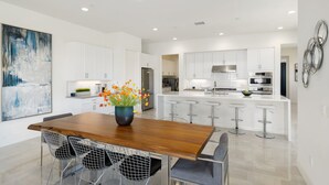 Una cocina moderna con armarios blancos, electrodomésticos de acero inoxidable y una isla central con taburetes de bar.