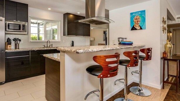 Una cocina moderna con armarios oscuros, una campana extractora de acero inoxidable, un microondas y una isla grande con taburetes de bar.