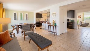 Amplia sala de estar con sofá, reposapiés y mesa de comedor, que da a una cocina con electrodomésticos modernos y una isla visible.