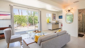 A modern living room with a glass coffee table, grey sofa, and a view of the outdoors through large sliding doors. - Lux Desert Retreat 4BR Pool Spa Stunning Views (Palm Springs)