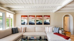 A modern living room with a beige sectional sofa, a glass coffee table, and a large window. - Movie Colony Oasis - Peaceful Walk to Downtown (Palm Springs)