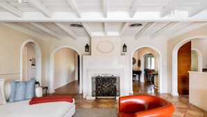 A spacious living room with a fireplace, a sofa, and a red chair. There are multiple archways and a dining area in the background. - Movie Colony Oasis - Peaceful Walk to Downtown (Palm Springs)