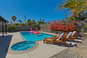 A swimming pool with a hot tub, lounge chairs, and a stone wall with red flowers. - Modern Home w Private Pool Spa Pets Welcome (Palm Springs)