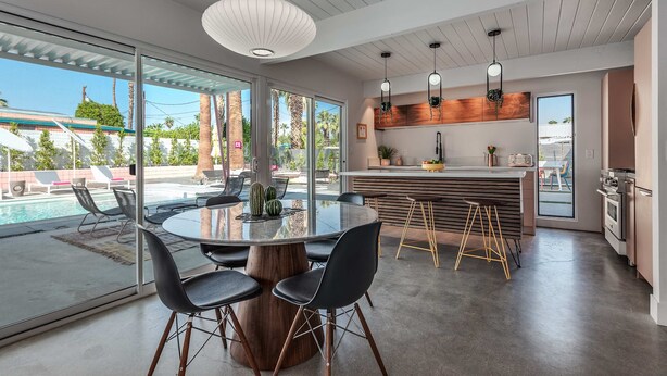Una cocina moderna con una isla central, taburetes de bar y vistas al área de la piscina exterior.