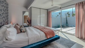 Un dormitorio moderno con una cama grande, un ventilador de techo y vistas a un jardín a través de un gran ventanal corredero.