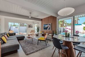 A modern living room with a sectional sofa, a dining table, and a pool view. - Retro Chic Oasis Saltwater Pool Spa Mnt Views (Palm Springs)