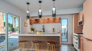 Una cocina moderna con una isla central, taburetes de bar, plantas colgantes y un amplio ventanal.
