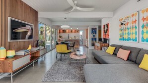 Una sala de estar moderna con un sofá gris, un sillón amarillo y un mueble de entretenimiento de madera con un televisor.