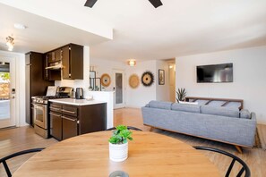 A modern kitchen with dark cabinets, a built-in oven, and a dining area with a wooden table and a potted plant. - Near JT Oasis Hot Tub Cowboy Tub Games (Joshua Tree)