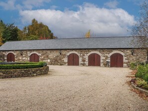 Set amidst lush greenery, this charming stone building offers a serene entrance with a gravel driveway and arched doors.