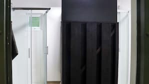 Una habitación con una puerta de vidrio que da a un área de ducha, un mueble negro y una pared blanca.