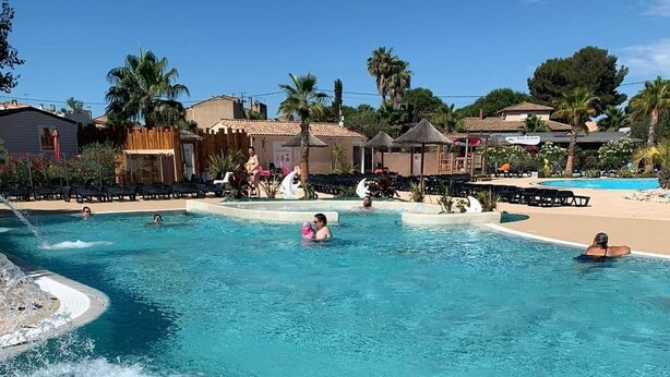 A large outdoor swimming pool with clear blue water, surrounded by lounge chairs and palm trees. - CAP VALRAS Les sables du midi (Valras-Plage)