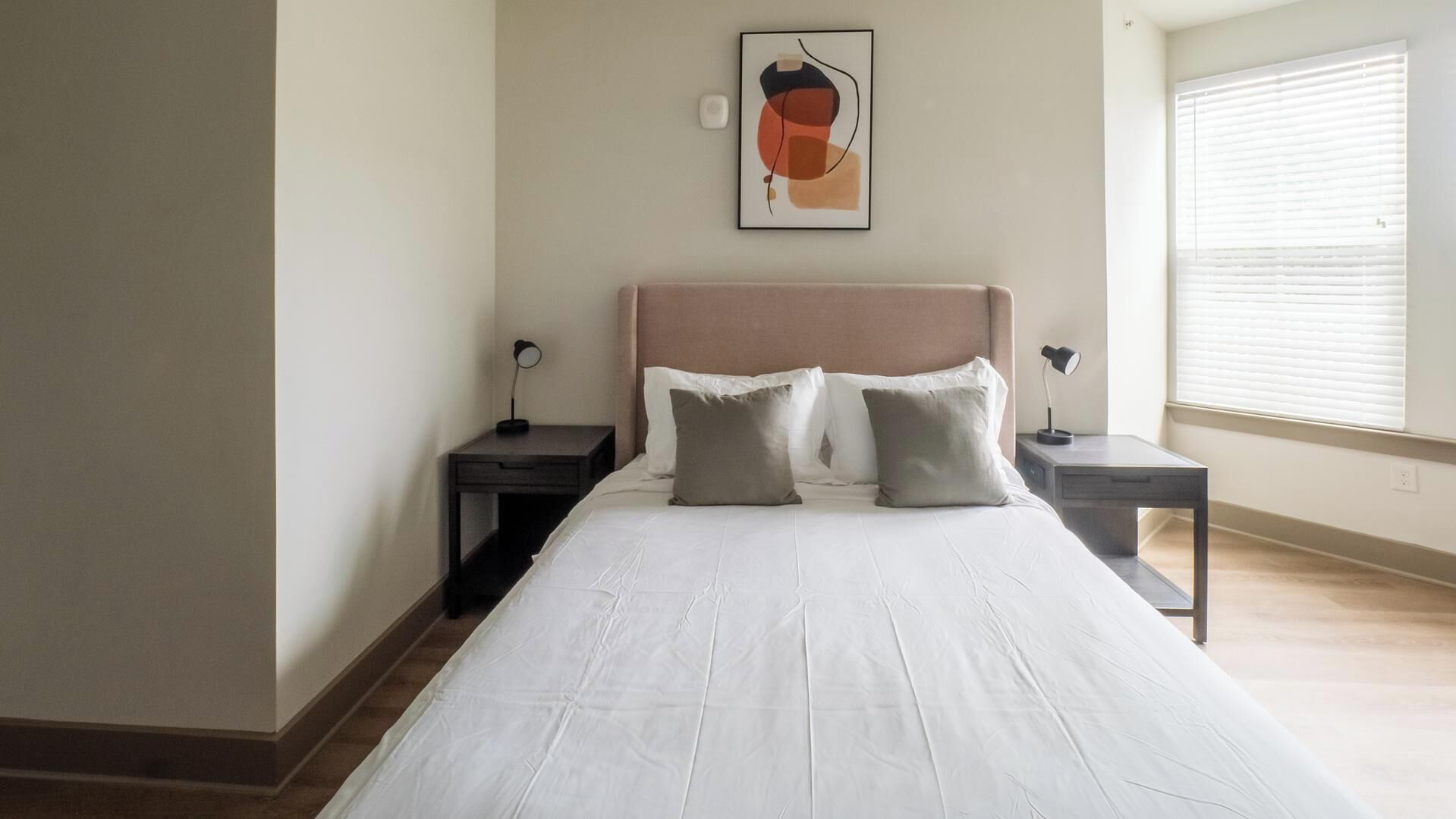 Ein Schlafzimmer mit einem Bett, zwei Nachttischen, einer Wandleuchte und einem Fenster mit Jalousien.