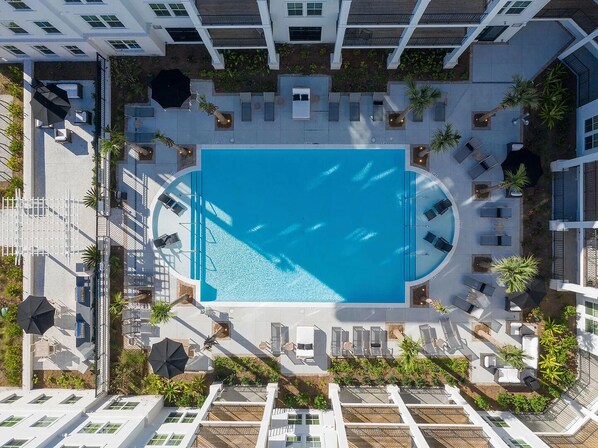 Vista aérea de un hotel con piscina central, tumbonas y jardín en la azotea.