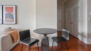 Una sala de estar moderna con una mesa redonda y dos sillas negras, un sofá blanco y un cuadro abstracto grande en la pared.