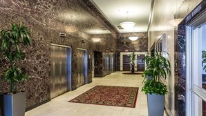 A marble-floored hallway with elevators, potted plants, and a patterned carpet.