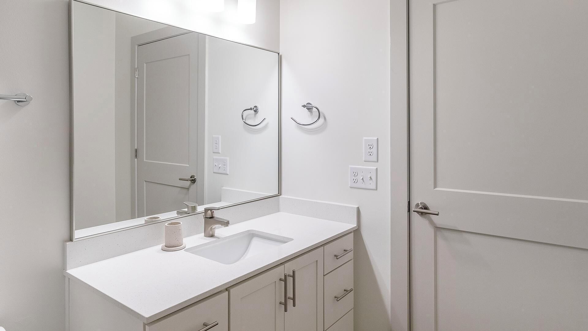 Ein modernes Badezimmer mit Waschbecken, Spiegel und Schränken, alles in Weiß.