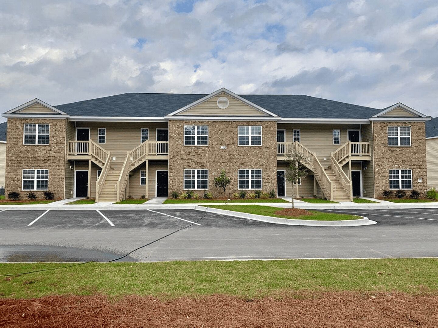 A multi-story apartment building with a central entrance, balconies, and a parking lot in front.
