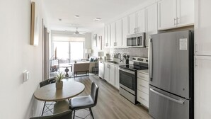 A modern kitchen with stainless steel appliances, a dining area with a round table and chairs, and a view to the outside. - Landing | Modern 1BD, Gym, Clubhouse (Huntsville)